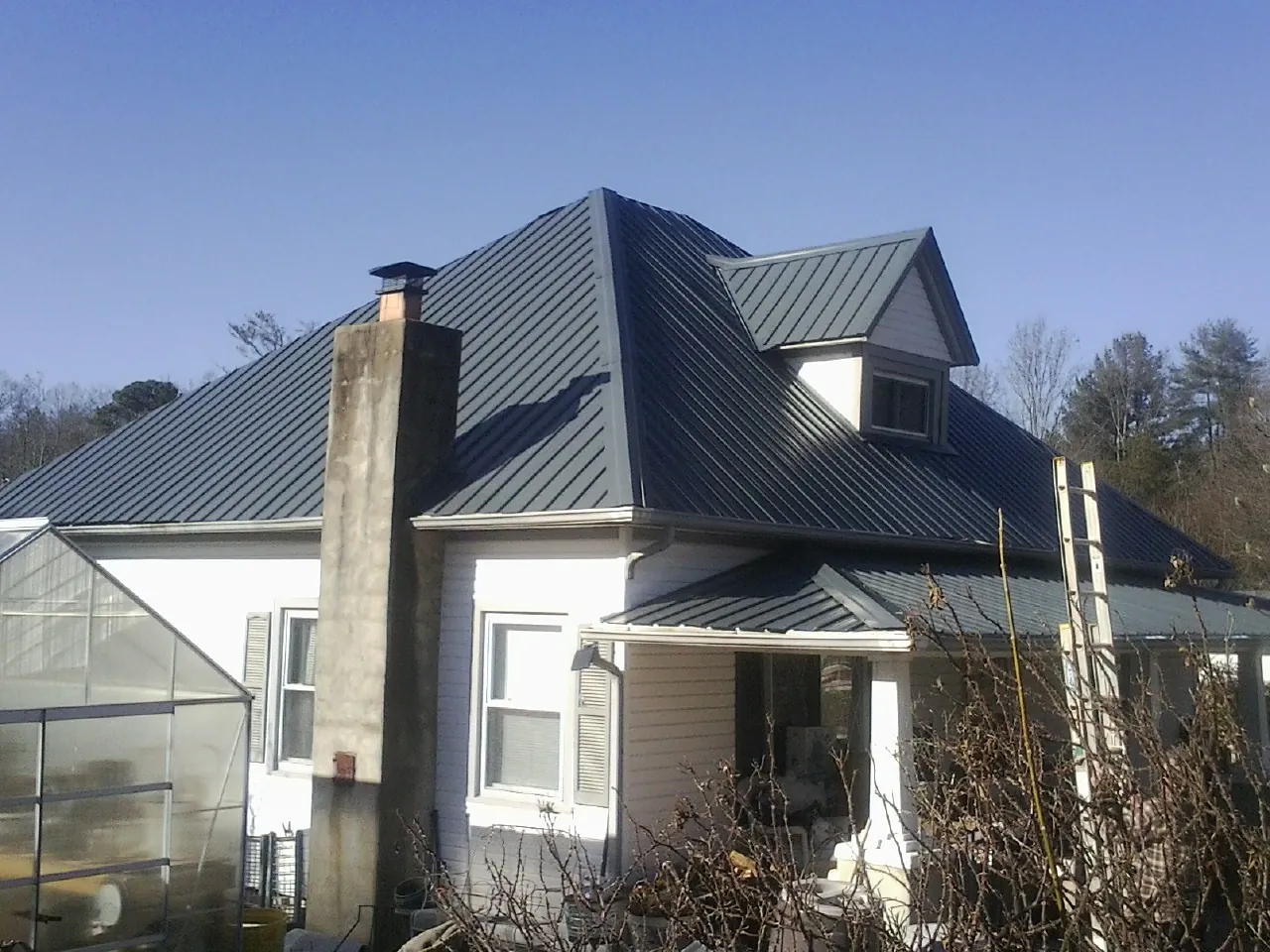 Dark blue standing seam metal roof on a white farmhouse with dormer — Slate & Tile Roof Repair by Roofing Brothers in Glenmont
