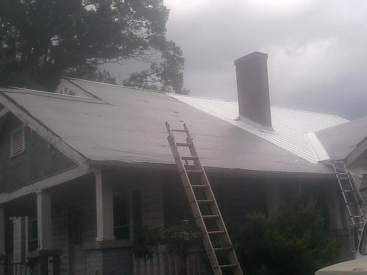 Ladders against a metal roof on an older home with a brick chimney in Glenmont