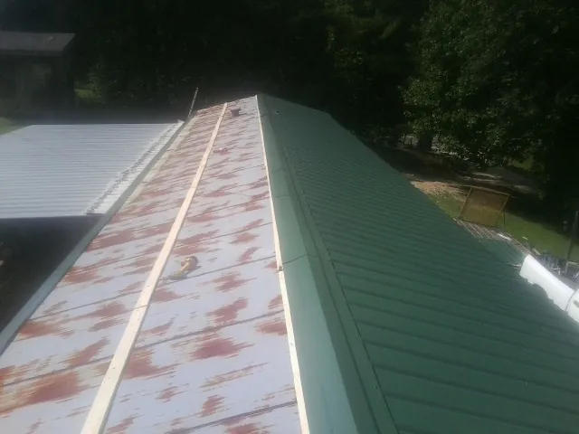 Old rusted panels beside newly installed green metal roofing — Wind Damage Roof Repair by Roofing Brothers in Glenmont