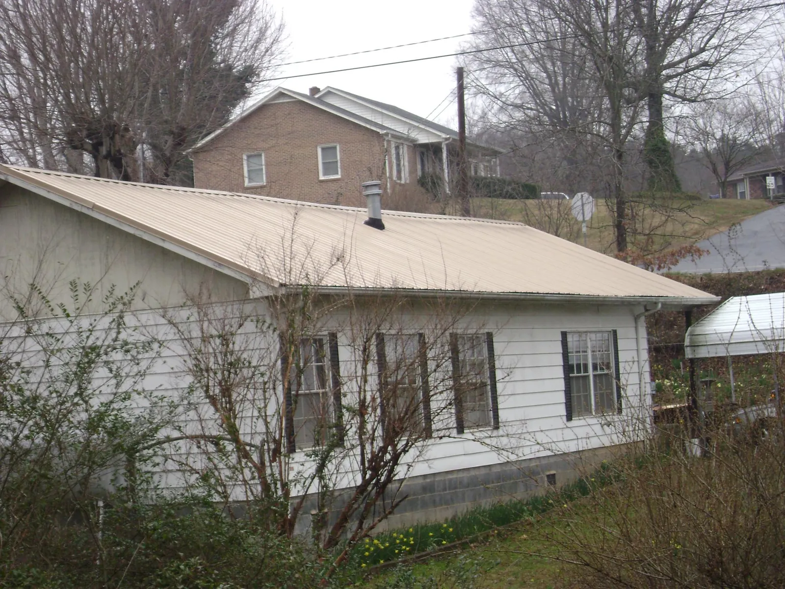 Tan metal roof on a white sided house set into a hillside — Commercial Roofing by Roofing Brothers in Glenmont